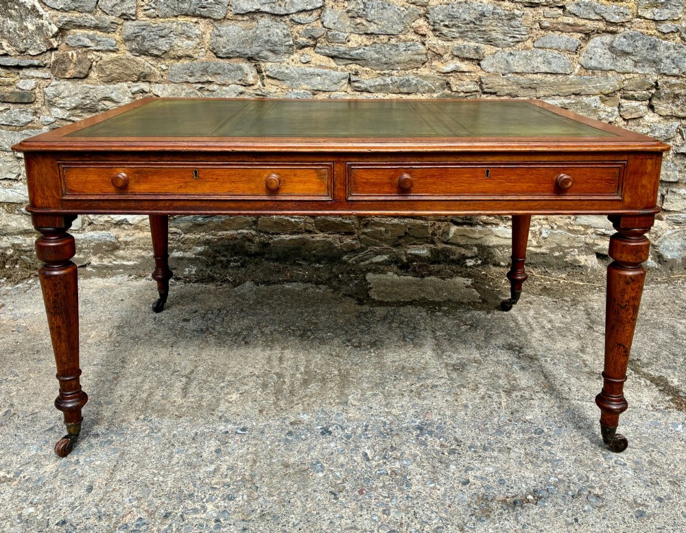 A Victorian oak writing desk featuring a green leather insert top, frieze drawers with wooden turned knobs, and turned legs with brass castors. View III