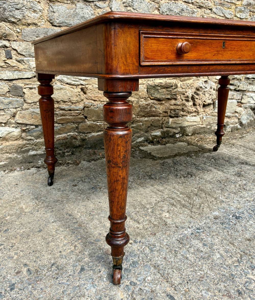 A Victorian oak writing desk featuring a green leather insert top, frieze drawers with wooden turned knobs, and turned legs with brass castors. View V