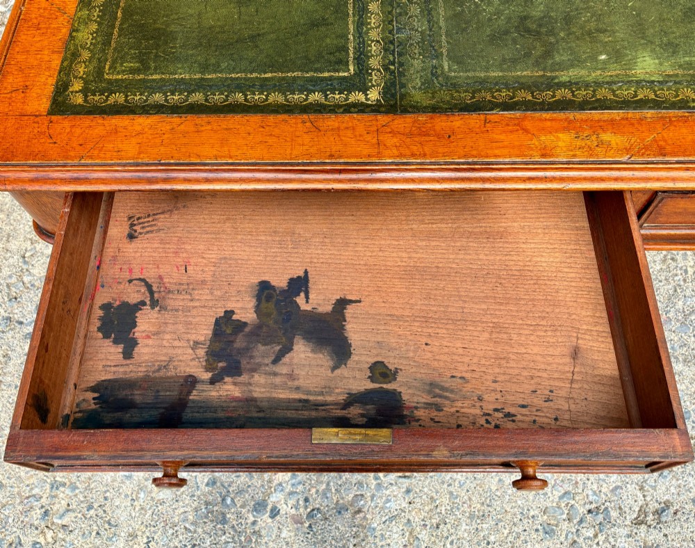 A Victorian oak writing desk featuring a green leather insert top, frieze drawers with wooden turned knobs, and turned legs with brass castors. View VII