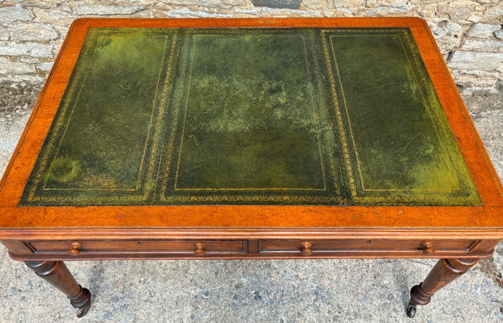 A Victorian oak writing desk featuring a green leather insert top, frieze drawers with wooden turned knobs, and turned legs with brass castors. View VIII