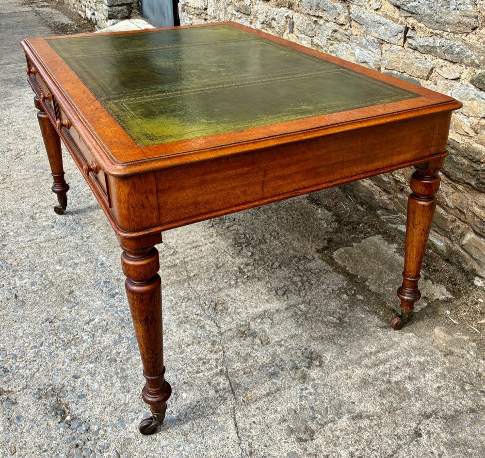 A Victorian oak writing desk featuring a green leather insert top, frieze drawers with wooden turned knobs, and turned legs with brass castors. View X