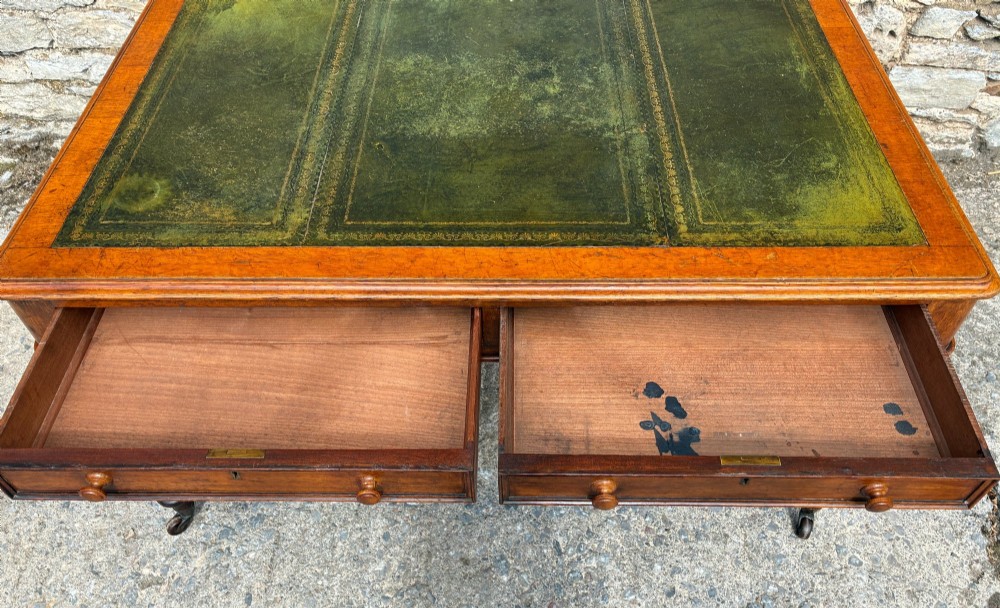 A Victorian oak writing desk featuring a green leather insert top, frieze drawers with wooden turned knobs, and turned legs with brass castors. View XII
