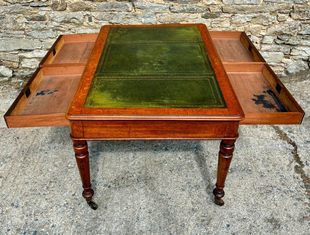 A Victorian oak writing desk featuring a green leather insert top, frieze drawers with wooden turned knobs, and turned legs with brass castors. View XV