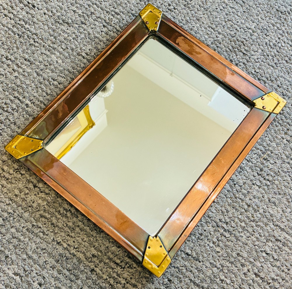 A rectangular wall mirror featuring a sheet copper frame reinforced with riveted brass corner plates. View II