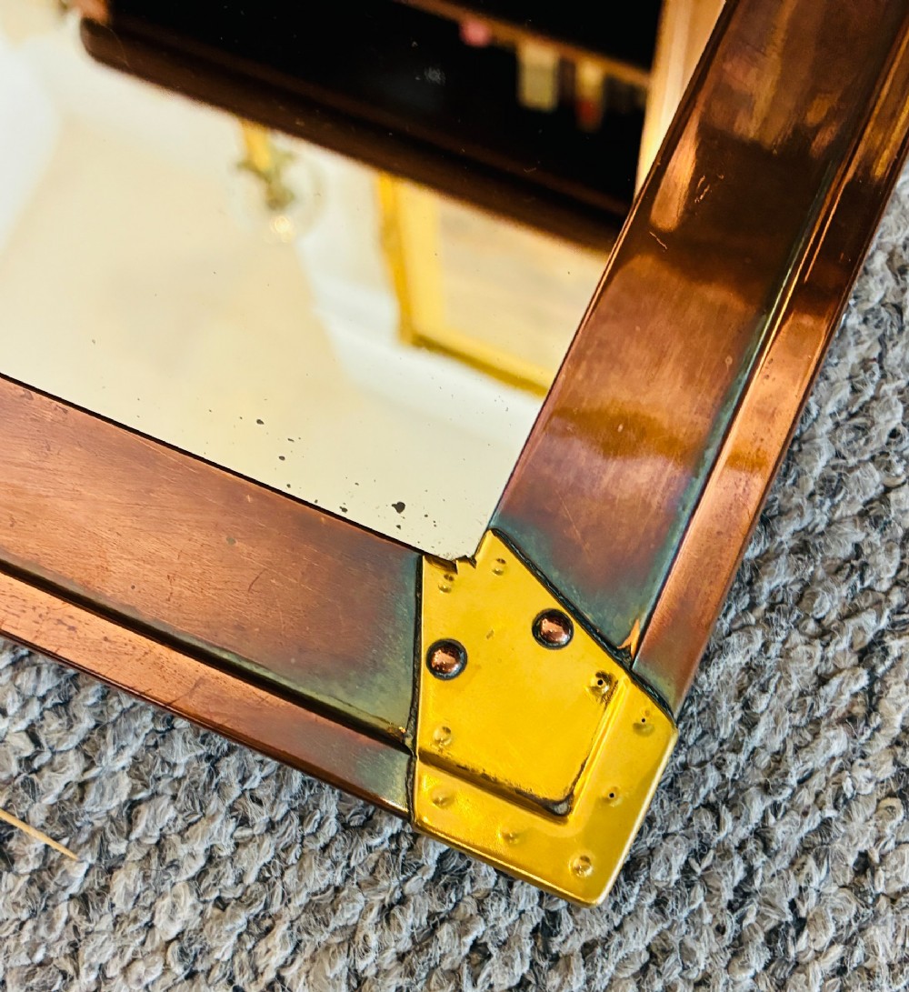 A rectangular wall mirror featuring a sheet copper frame reinforced with riveted brass corner plates. View VI