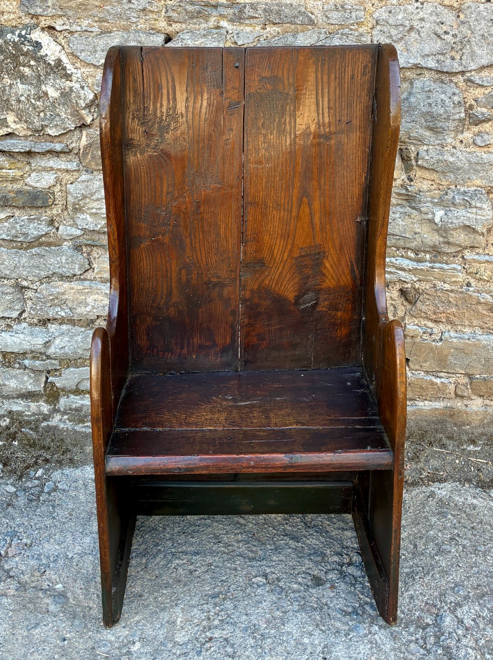 A dark oak primitive lambing chair featuring high winged sides, a tall two-panel back, a solid timber seat, and an enclosed box base.