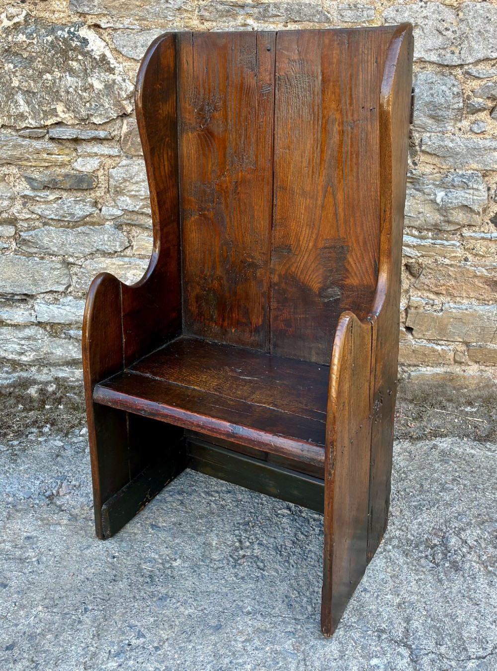 A dark oak primitive lambing chair featuring high winged sides, a tall two-panel back, a solid timber seat, and an enclosed box base. View III