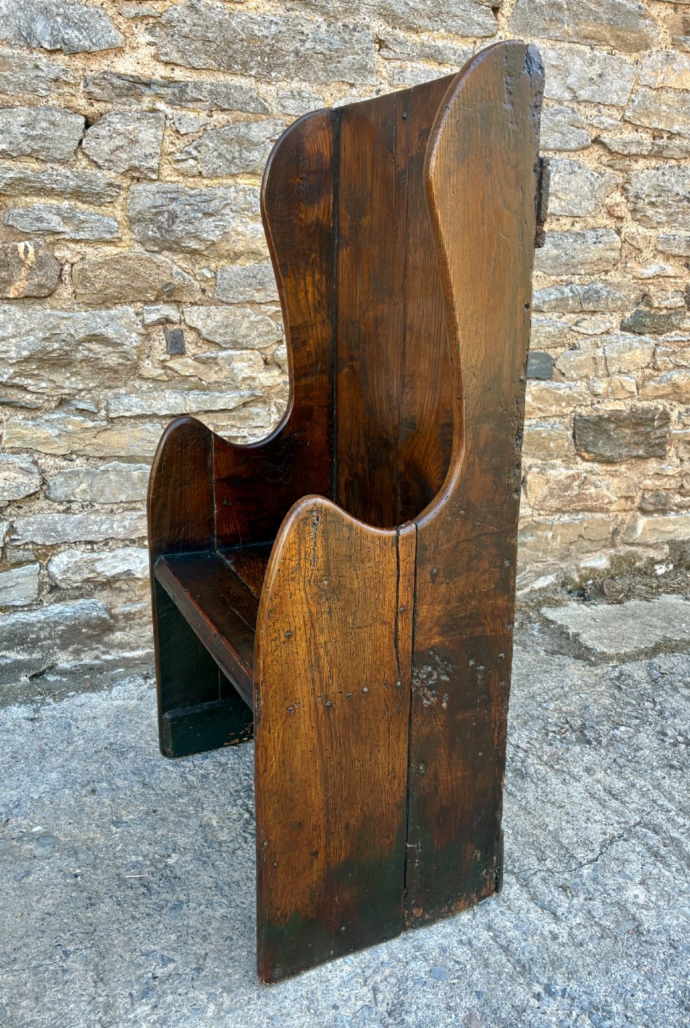 A dark oak primitive lambing chair featuring high winged sides, a tall two-panel back, a solid timber seat, and an enclosed box base. View IV