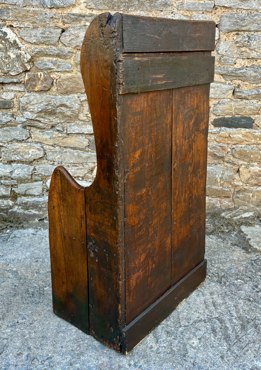 A dark oak primitive lambing chair featuring high winged sides, a tall two-panel back, a solid timber seat, and an enclosed box base. View V