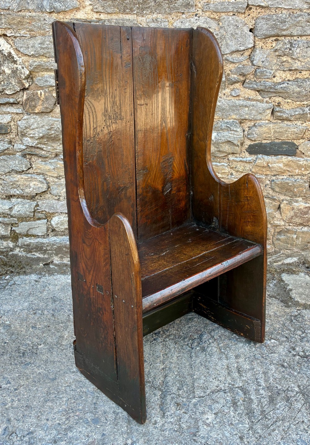 A dark oak primitive lambing chair featuring high winged sides, a tall two-panel back, a solid timber seat, and an enclosed box base. View XII