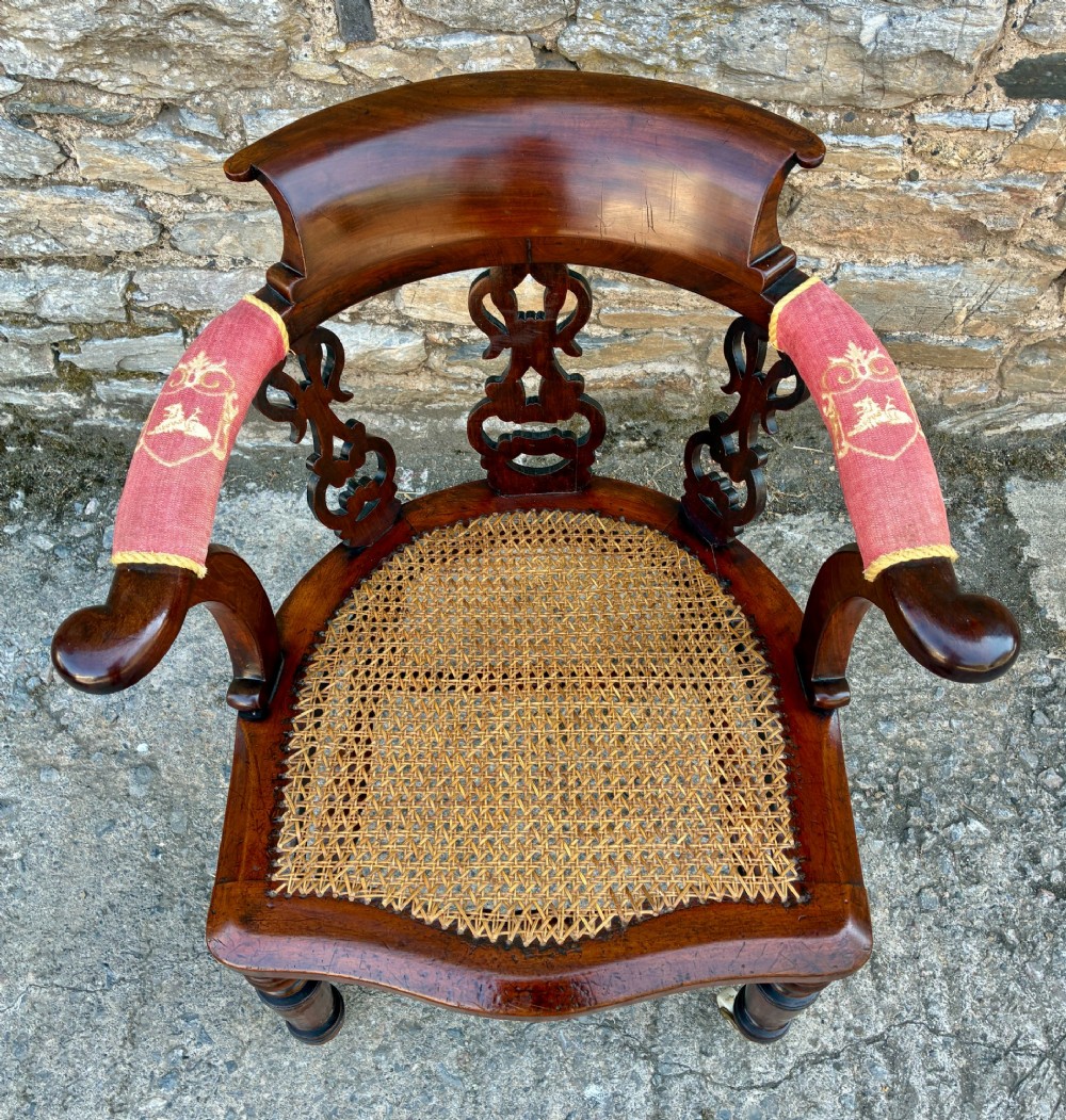 A Victorian mahogany desk chair featuring a curved top rail, pierced decorative splats, fabric-wrapped armrests, a woven cane seat, and turned legs with brass castors. View II