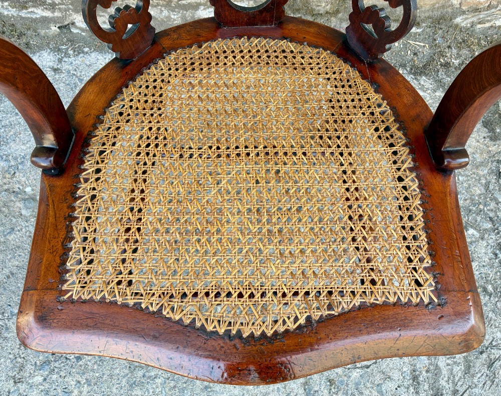 A Victorian mahogany desk chair featuring a curved top rail, pierced decorative splats, fabric-wrapped armrests, a woven cane seat, and turned legs with brass castors. View III