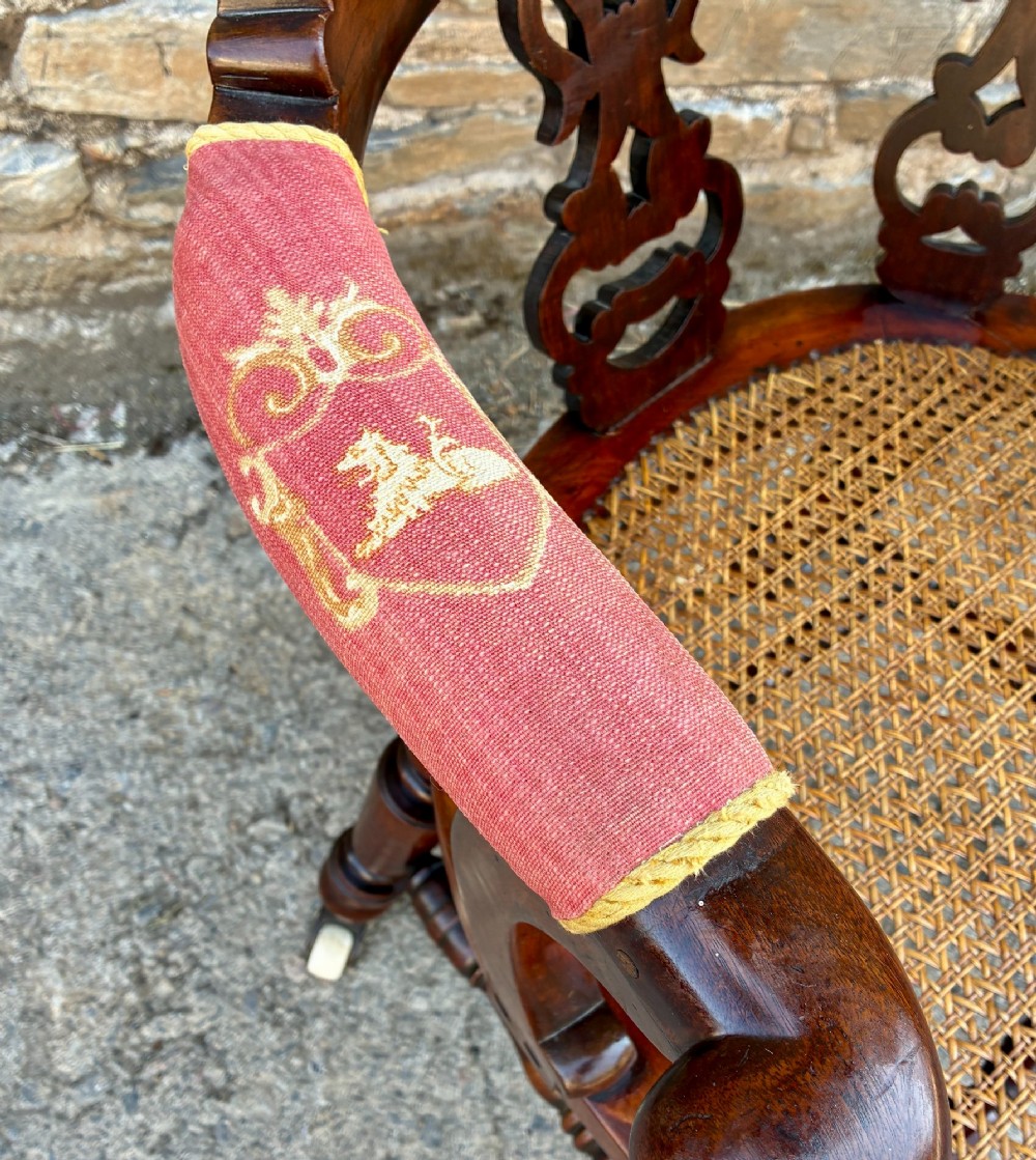A Victorian mahogany desk chair featuring a curved top rail, pierced decorative splats, fabric-wrapped armrests, a woven cane seat, and turned legs with brass castors. View XII
