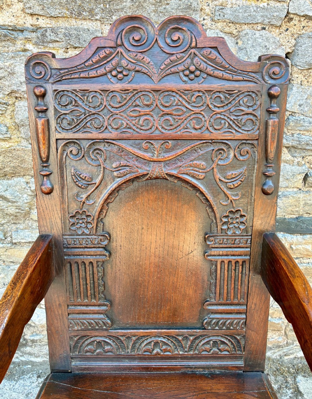 A dark carved oak wainscot armchair with a sculpted cresting rail, detailed panel back, turned front legs, and wooden stretchers. View III