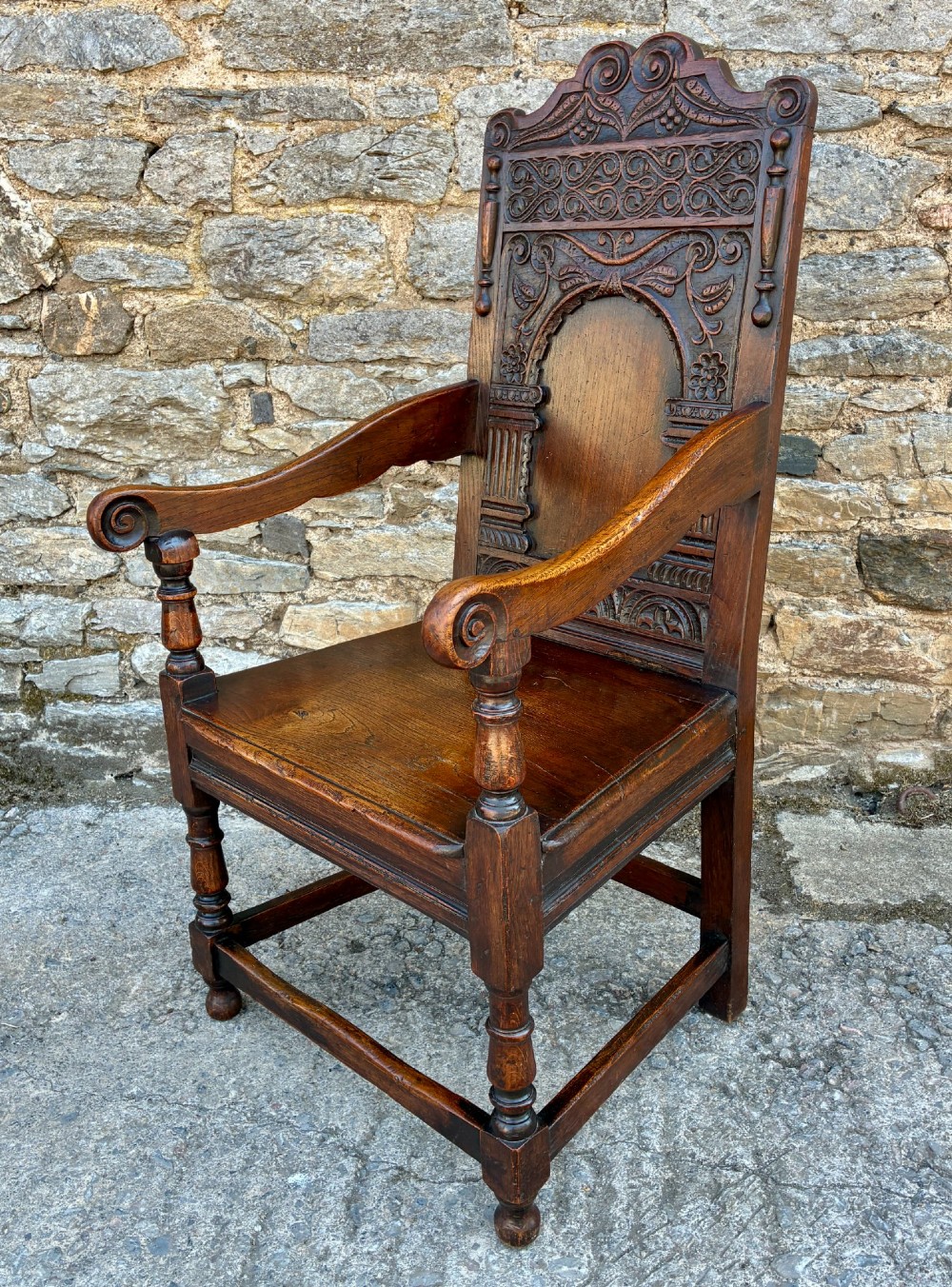 A dark carved oak wainscot armchair with a sculpted cresting rail, detailed panel back, turned front legs, and wooden stretchers. View IV