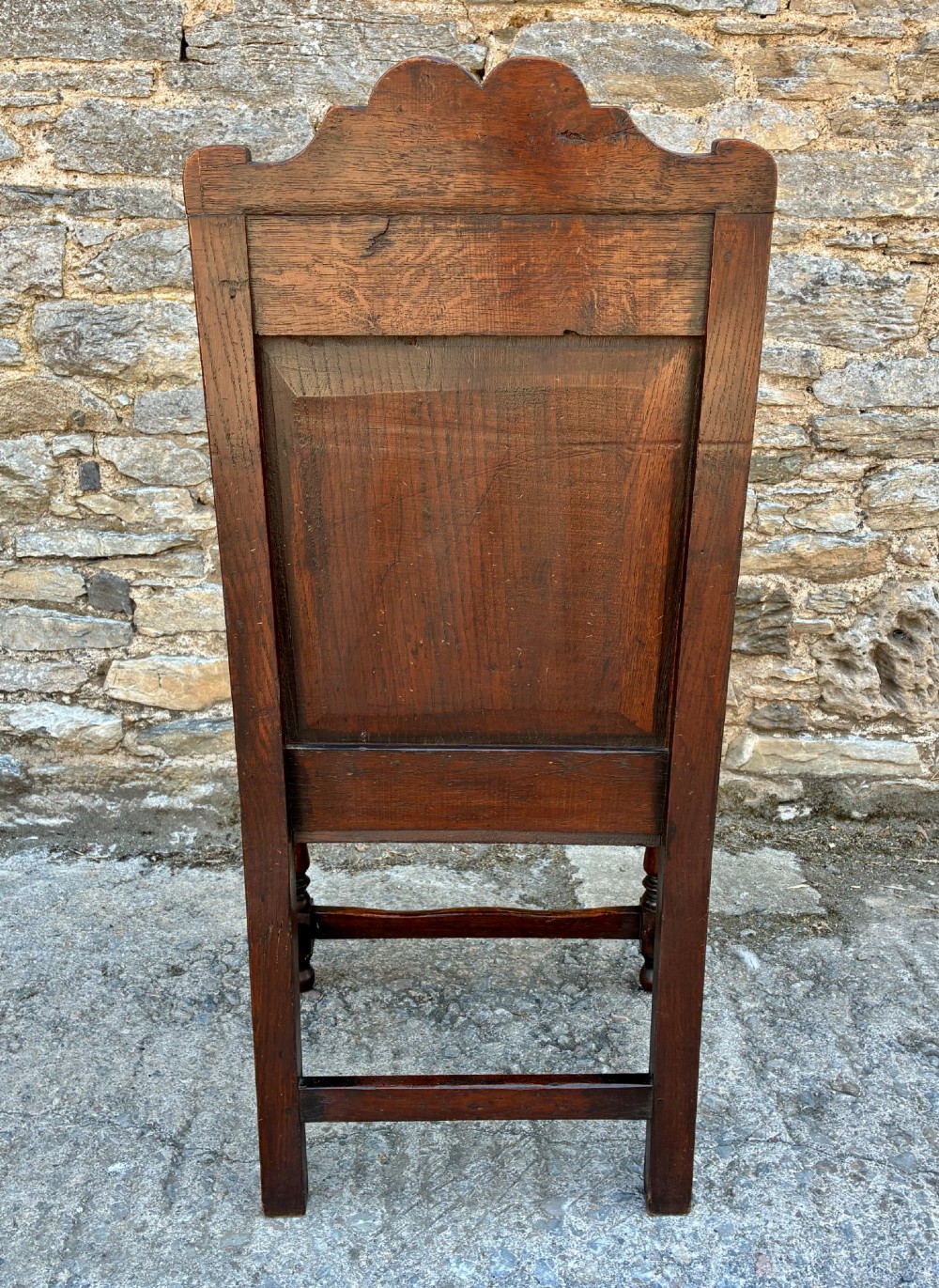 A dark carved oak wainscot armchair with a sculpted cresting rail, detailed panel back, turned front legs, and wooden stretchers. View VI