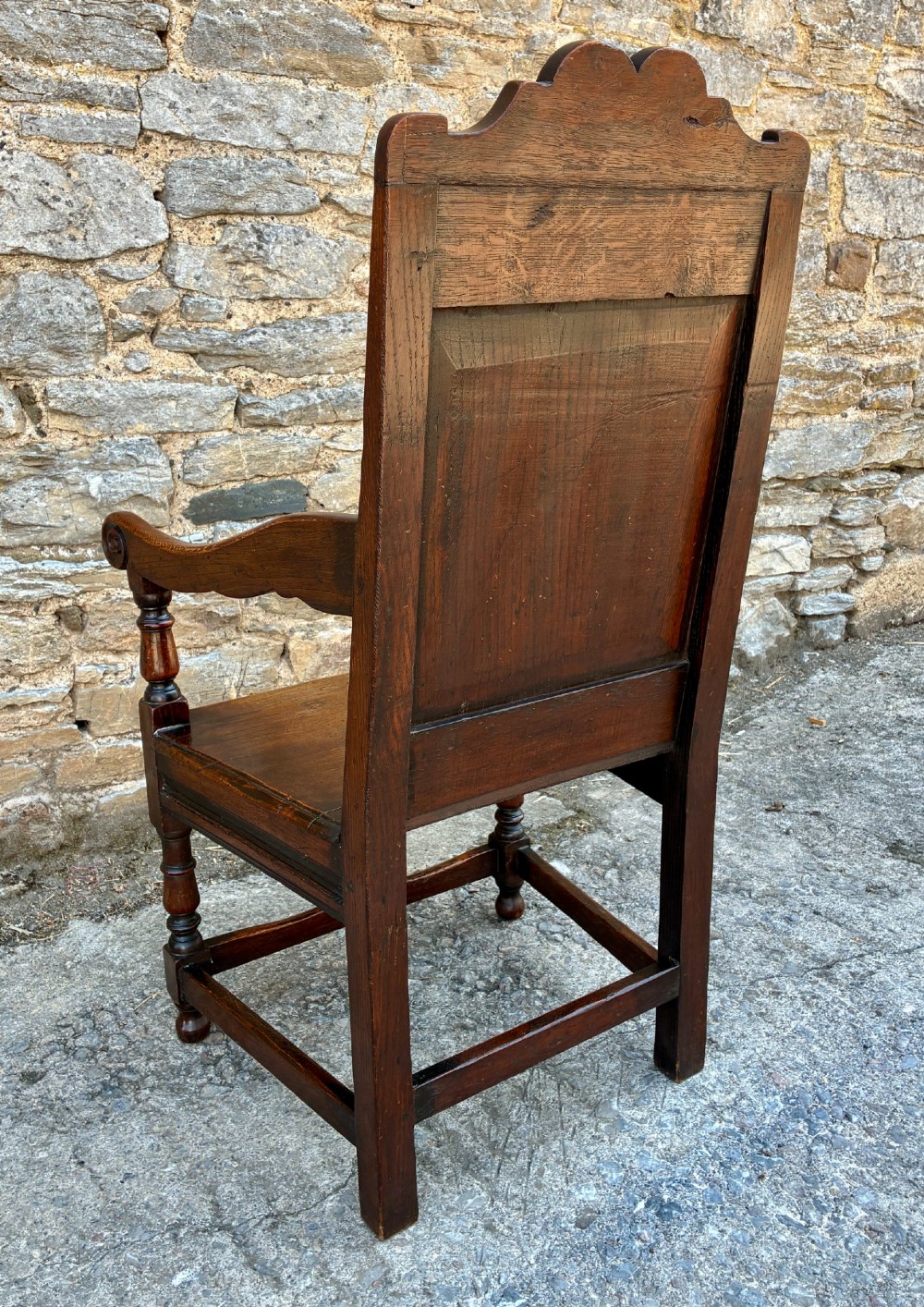 A dark carved oak wainscot armchair with a sculpted cresting rail, detailed panel back, turned front legs, and wooden stretchers. View VII