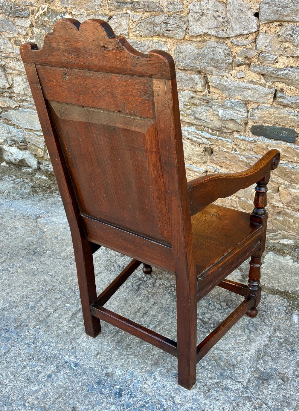 A dark carved oak wainscot armchair with a sculpted cresting rail, detailed panel back, turned front legs, and wooden stretchers. View VIII