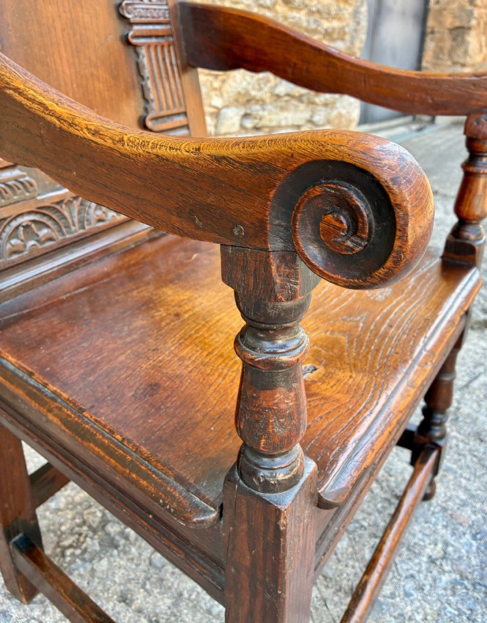 A dark carved oak wainscot armchair with a sculpted cresting rail, detailed panel back, turned front legs, and wooden stretchers. View XI