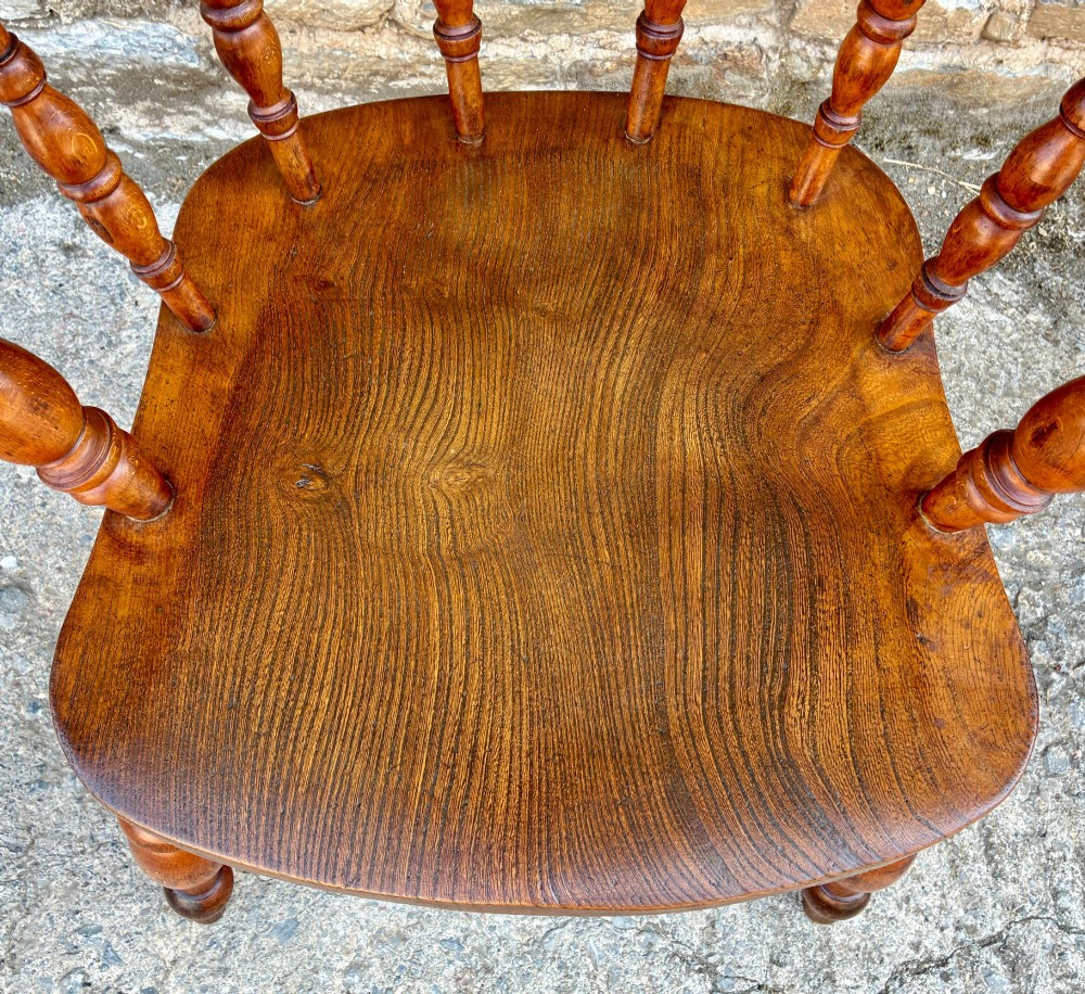 An antique wooden captains chair crafted from elm with turned spindles, a curved top rail, a contoured saddle seat, and turned legs. View II