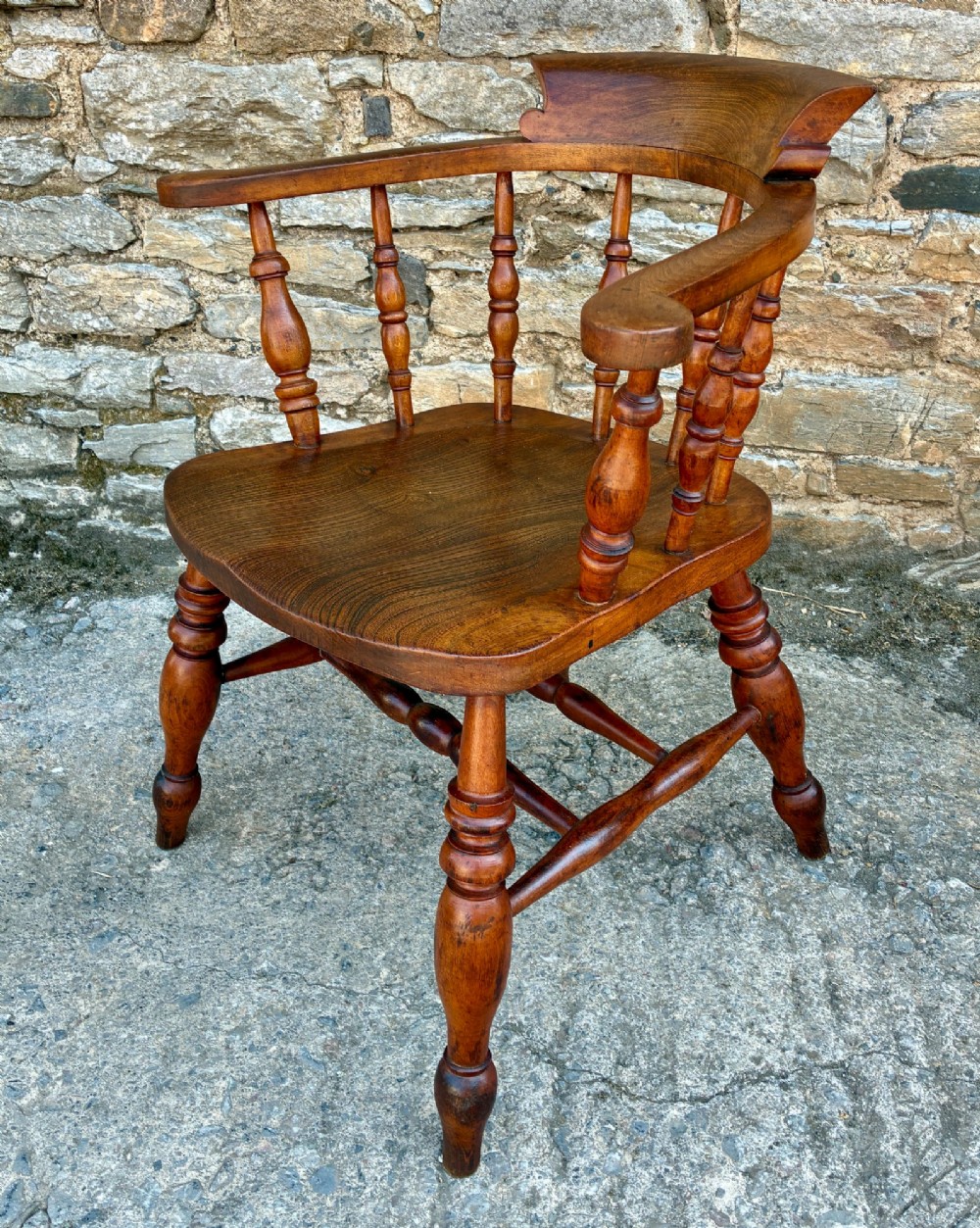 An antique wooden captains chair crafted from elm with turned spindles, a curved top rail, a contoured saddle seat, and turned legs. View III