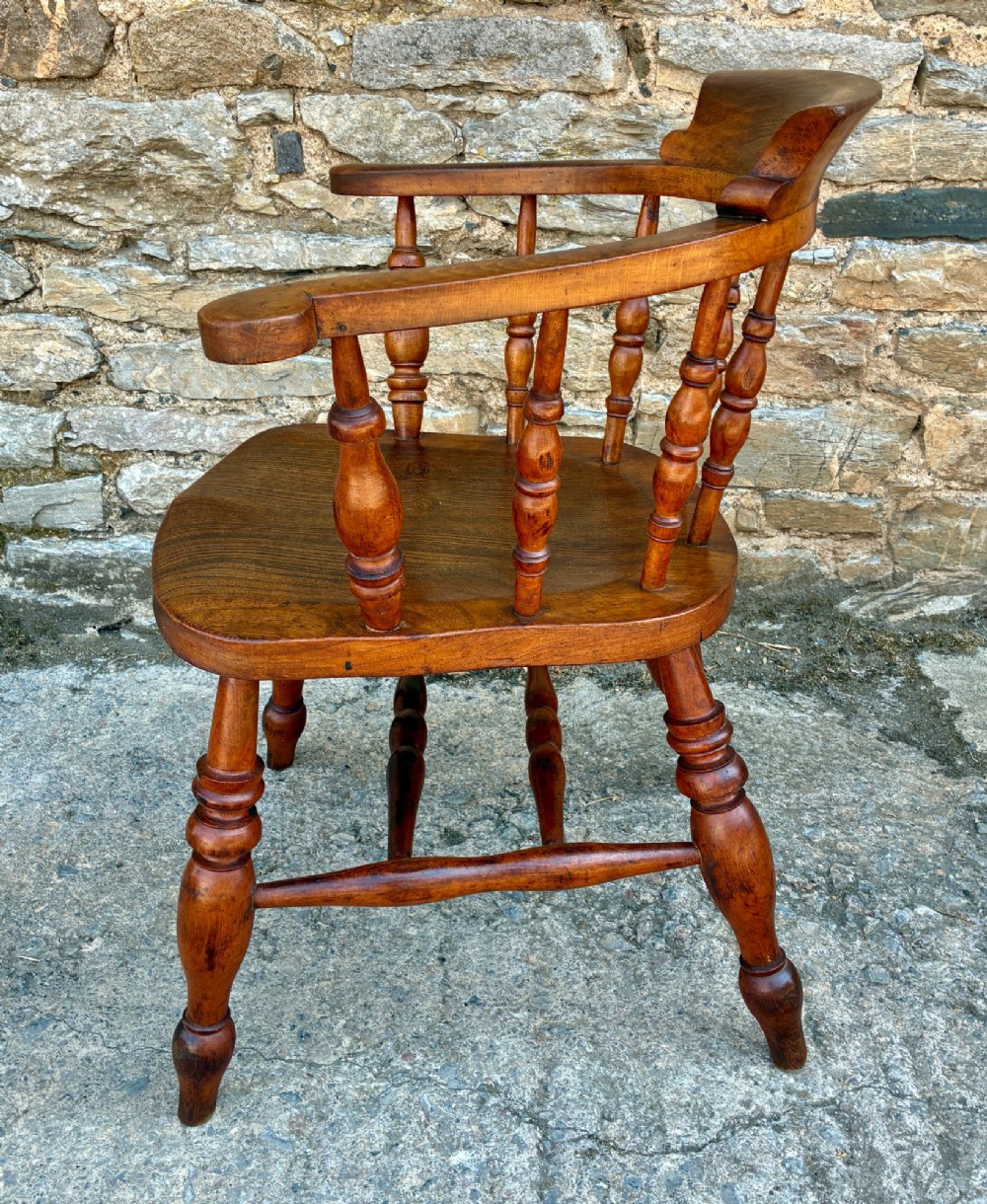 An antique wooden captains chair crafted from elm with turned spindles, a curved top rail, a contoured saddle seat, and turned legs. View IV