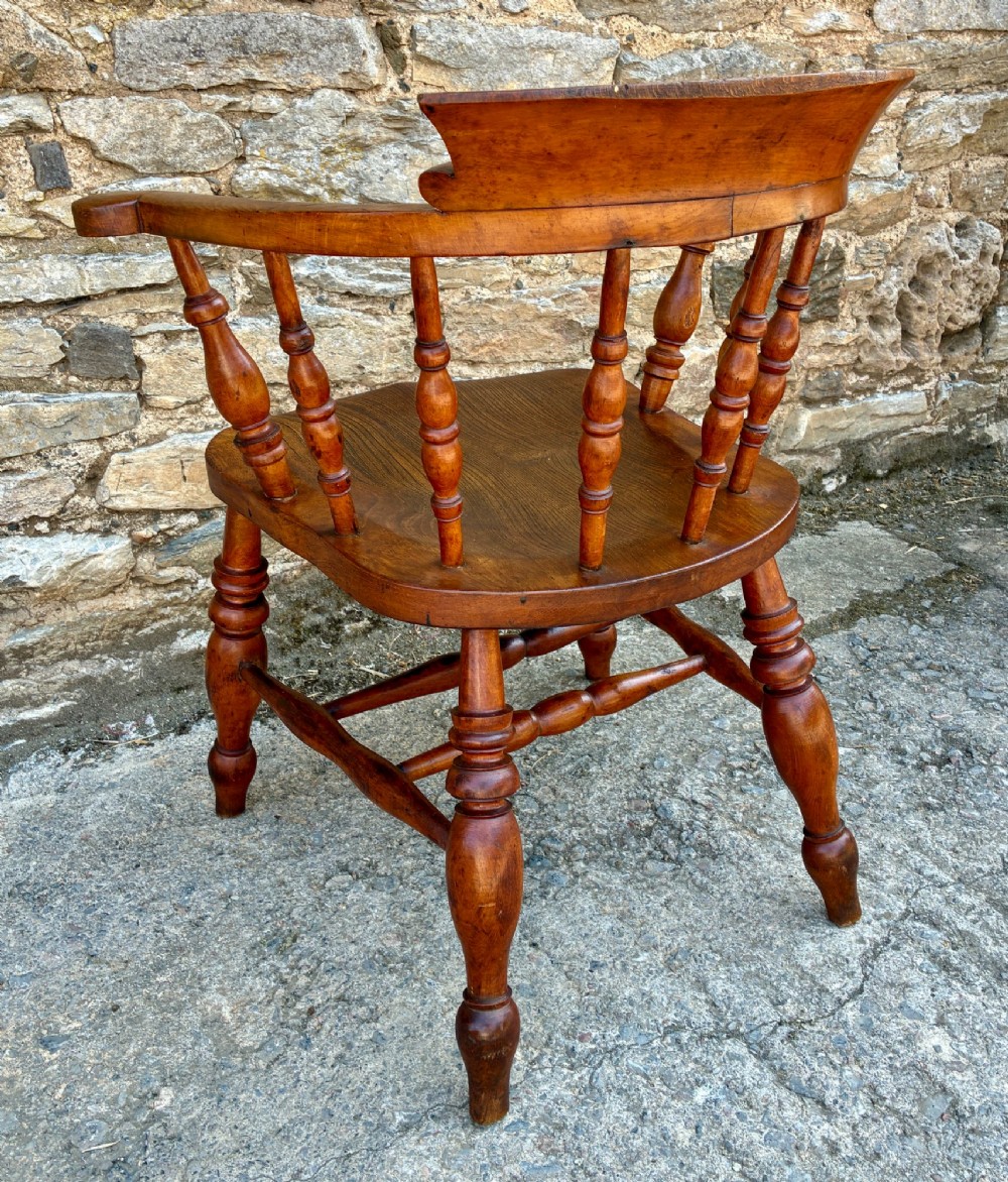 An antique wooden captains chair crafted from elm with turned spindles, a curved top rail, a contoured saddle seat, and turned legs. View VI