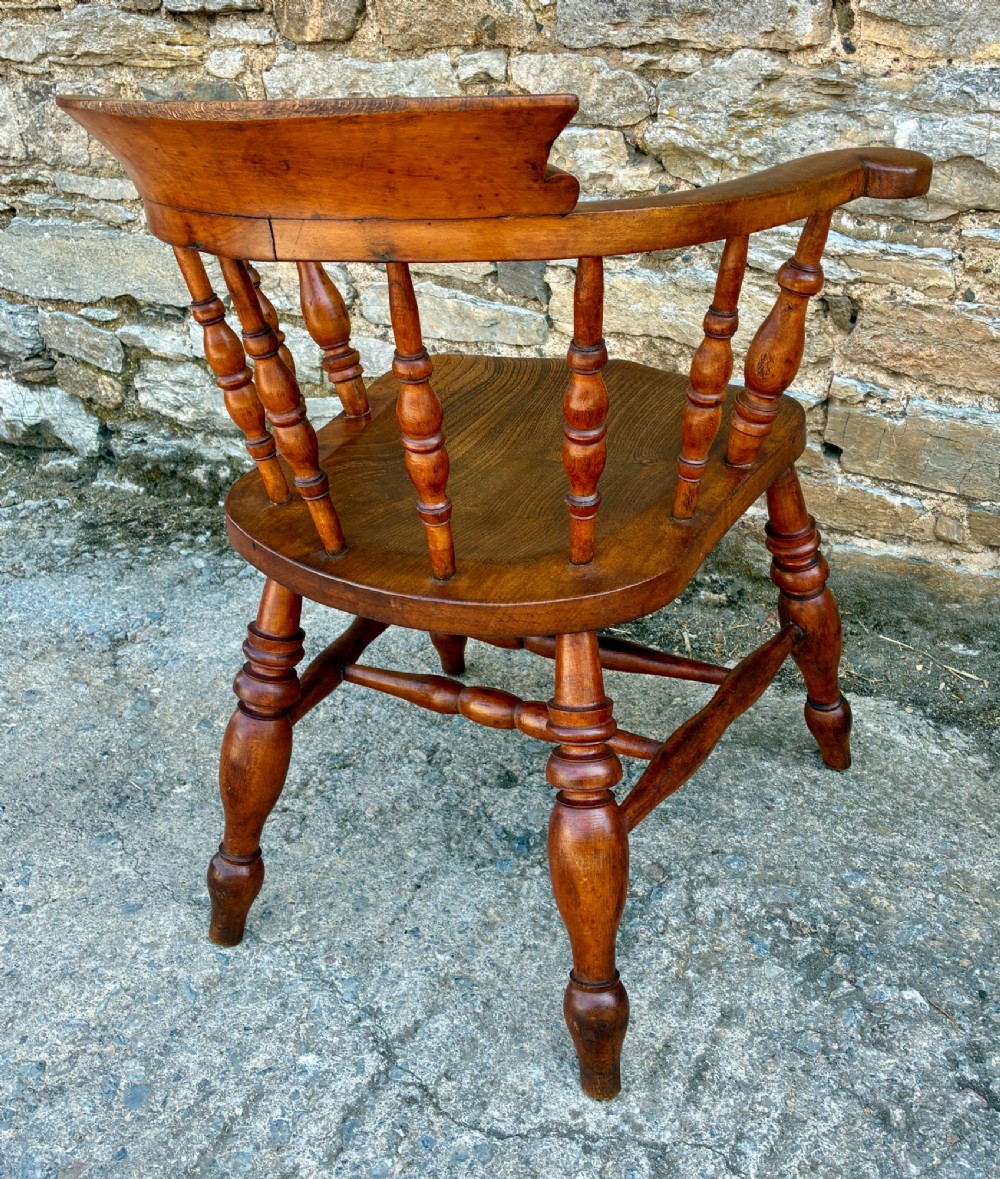 An antique wooden captains chair crafted from elm with turned spindles, a curved top rail, a contoured saddle seat, and turned legs. View VII