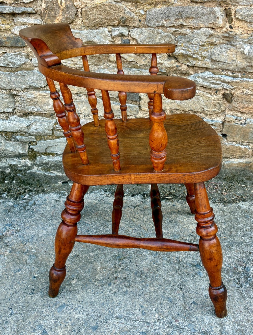 An antique wooden captains chair crafted from elm with turned spindles, a curved top rail, a contoured saddle seat, and turned legs. View IX