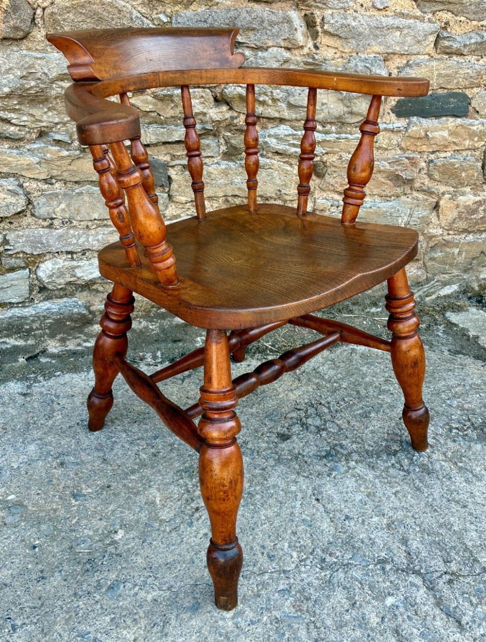 An antique wooden captains chair crafted from elm with turned spindles, a curved top rail, a contoured saddle seat, and turned legs. View X