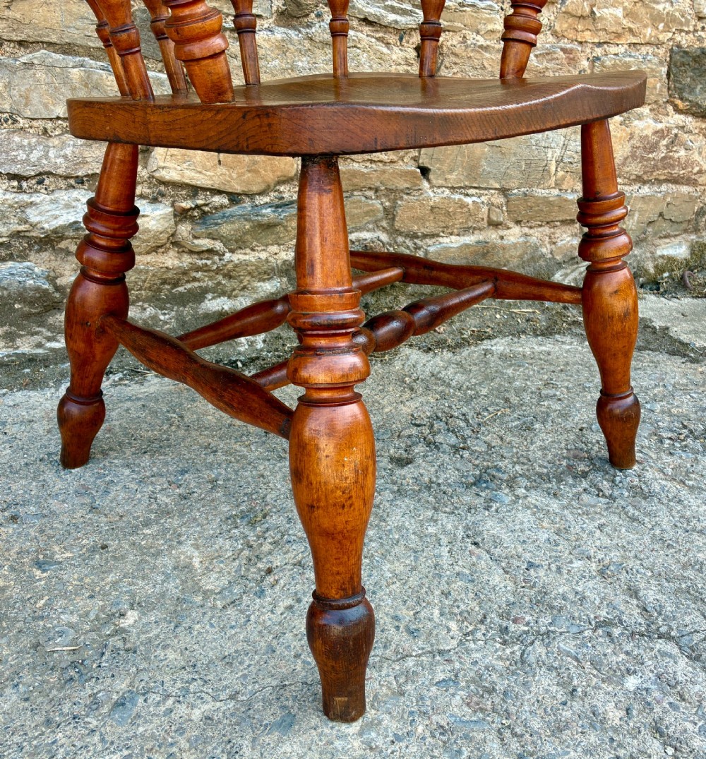An antique wooden captains chair crafted from elm with turned spindles, a curved top rail, a contoured saddle seat, and turned legs. View XI