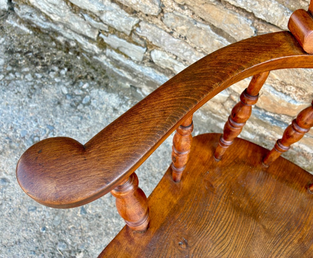 An antique wooden captains chair crafted from elm with turned spindles, a curved top rail, a contoured saddle seat, and turned legs. View XII