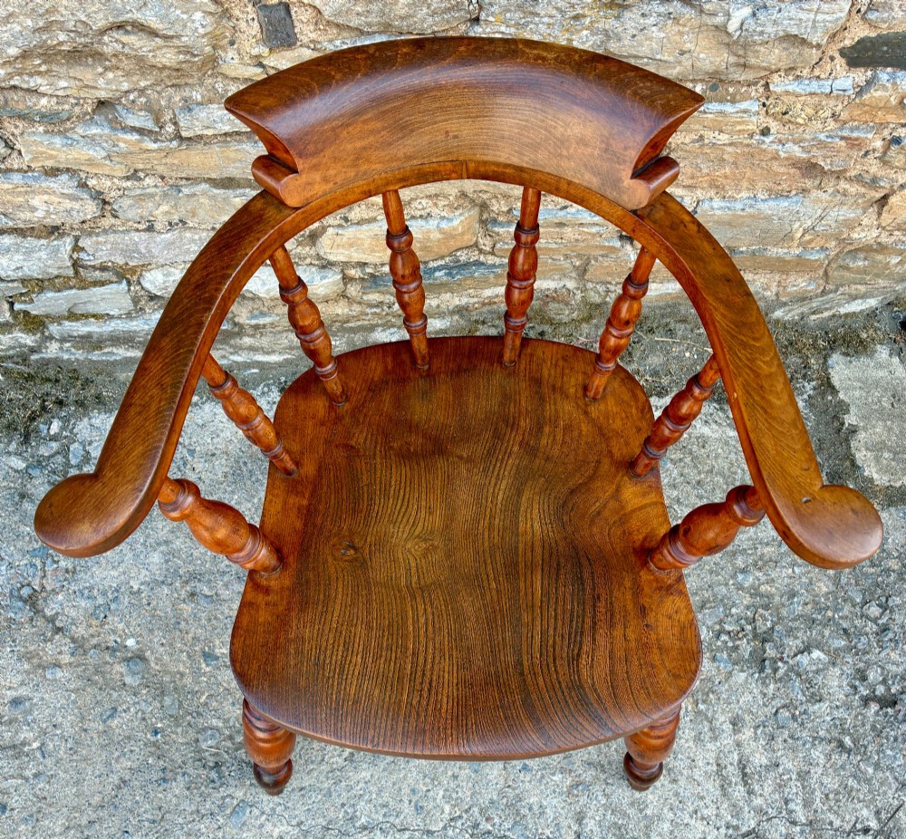 An antique wooden captains chair crafted from elm with turned spindles, a curved top rail, a contoured saddle seat, and turned legs. View XIII