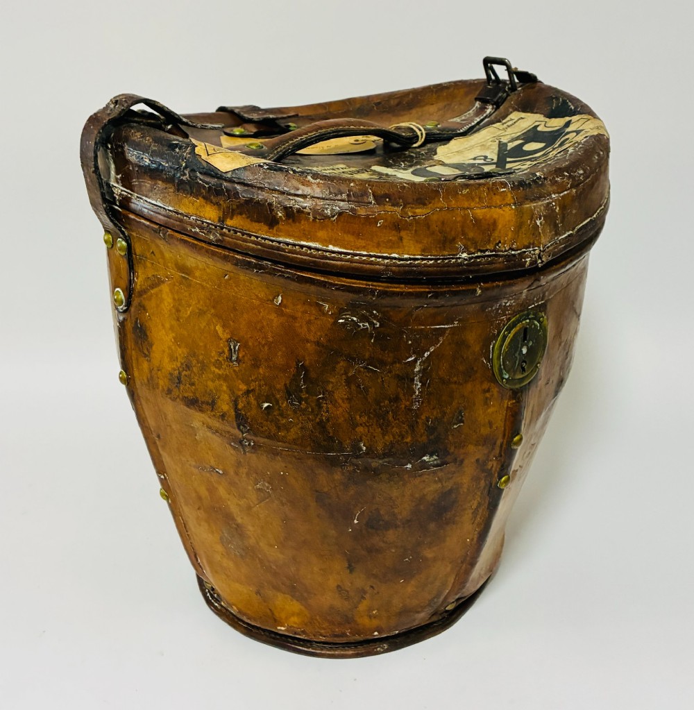 An antique tan leather double hat box featuring a shaped lid, top carrying handle, brass lock plate, and historical paper travel labels. View VII