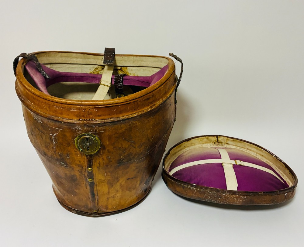 An antique tan leather double hat box featuring a shaped lid, top carrying handle, brass lock plate, and historical paper travel labels. View VIII