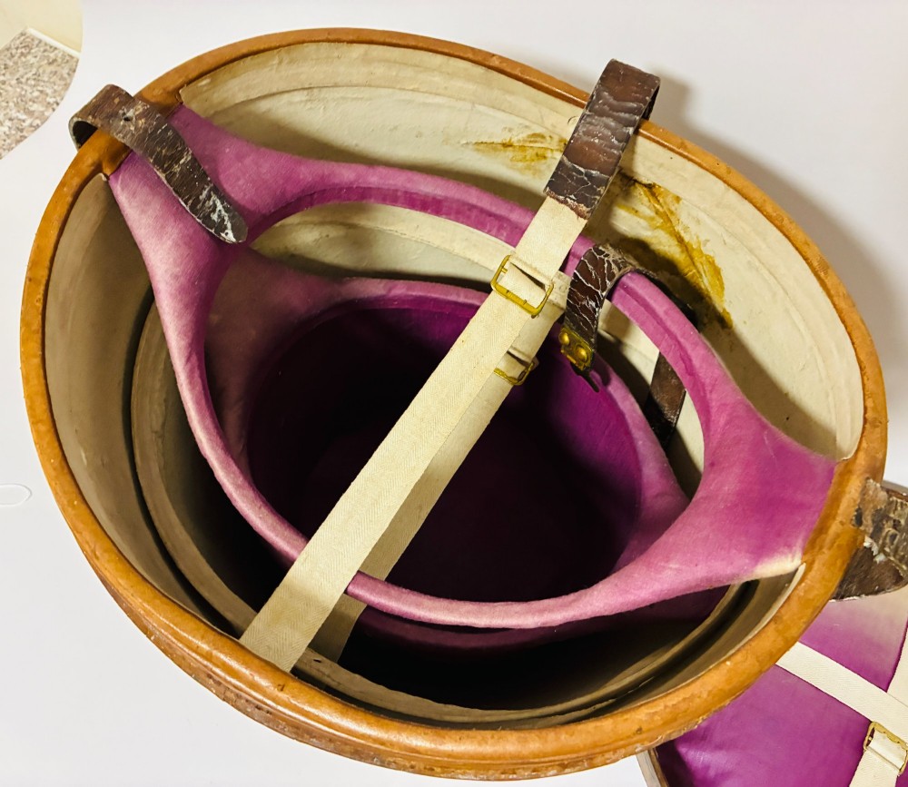 An antique tan leather double hat box featuring a shaped lid, top carrying handle, brass lock plate, and historical paper travel labels. View IX
