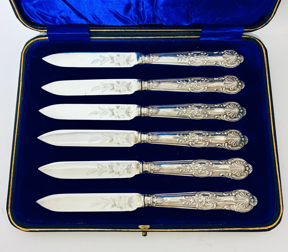 A cased set of six silver-handled fruit knives with floral engraved blades, displayed inside a blue velvet-lined presentation box. View II