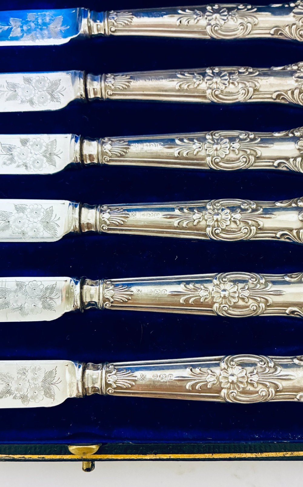 A cased set of six silver-handled fruit knives with floral engraved blades, displayed inside a blue velvet-lined presentation box. View V