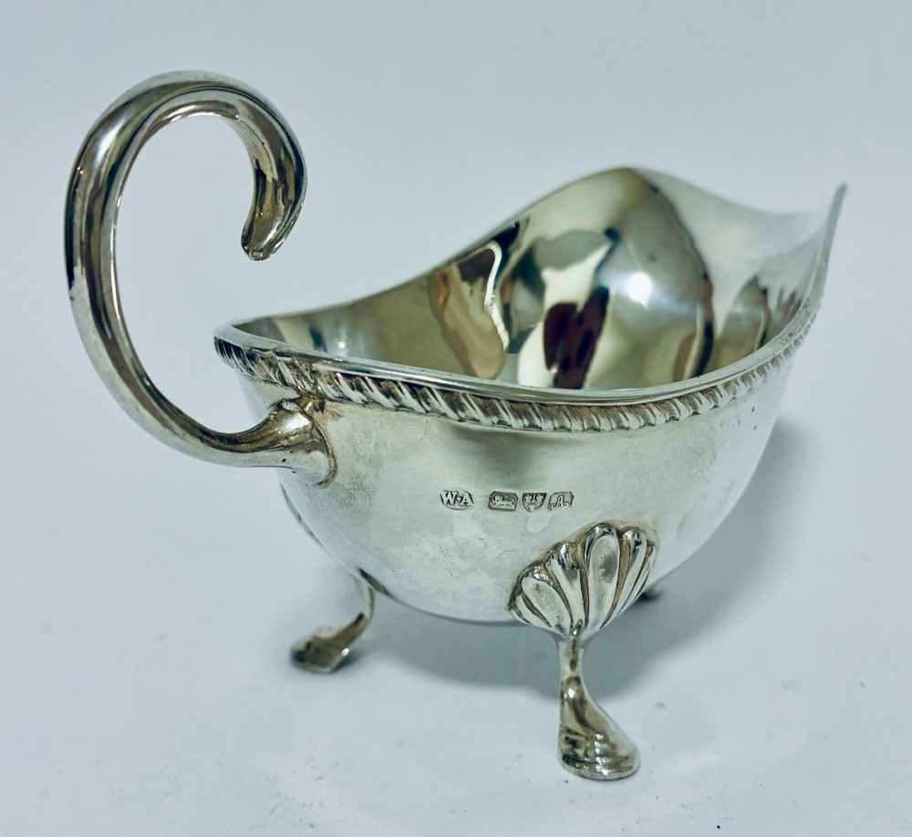 A polished sterling silver sauce boat featuring a flying scroll handle, gadrooned border, and three shell-capped pad feet. View II