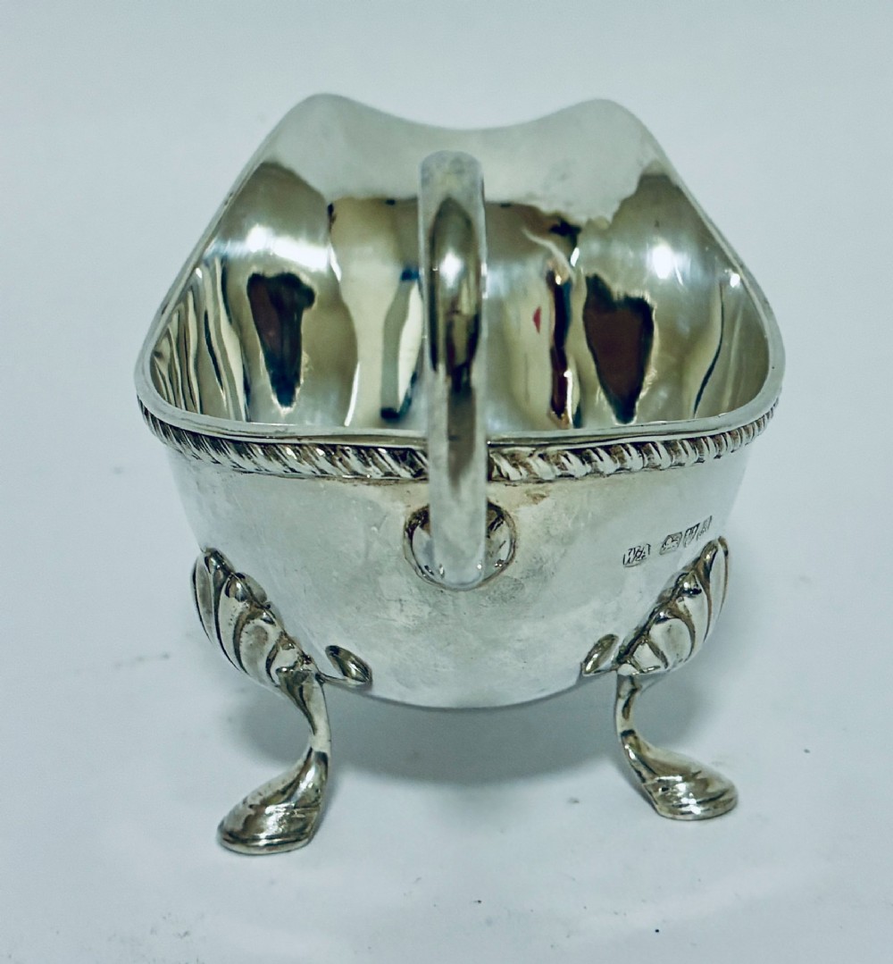 A polished sterling silver sauce boat featuring a flying scroll handle, gadrooned border, and three shell-capped pad feet. View III