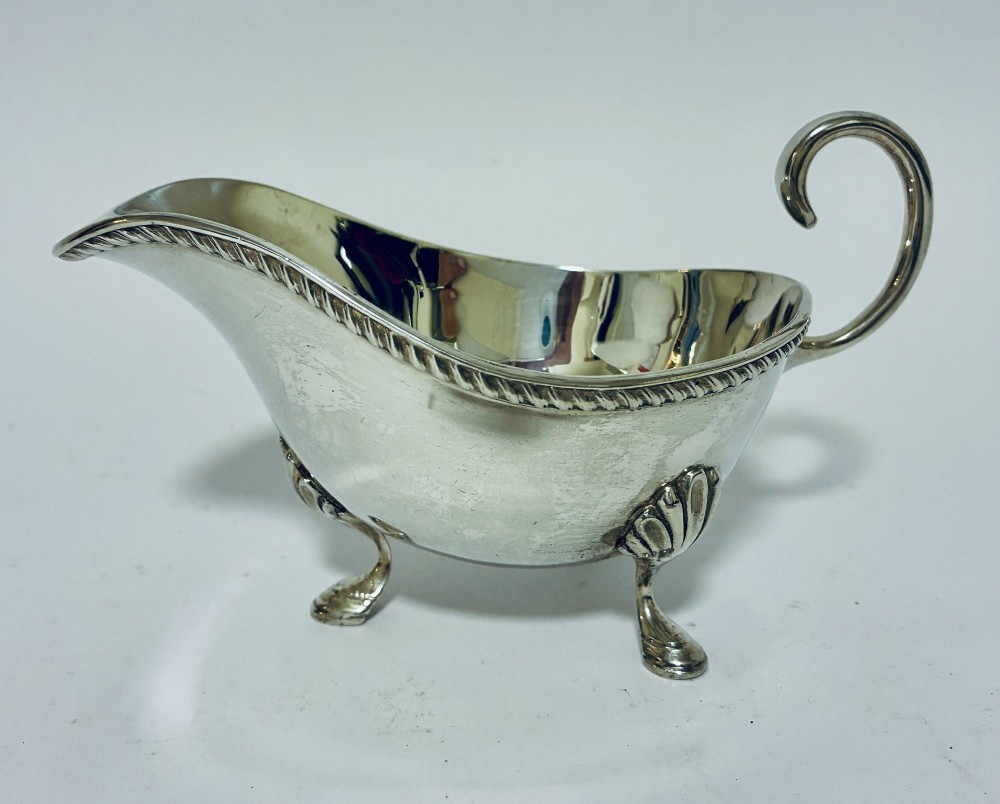 A polished sterling silver sauce boat featuring a flying scroll handle, gadrooned border, and three shell-capped pad feet. View IV