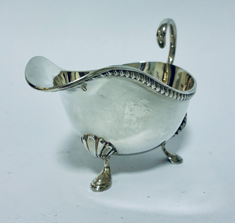 A polished sterling silver sauce boat featuring a flying scroll handle, gadrooned border, and three shell-capped pad feet. View V