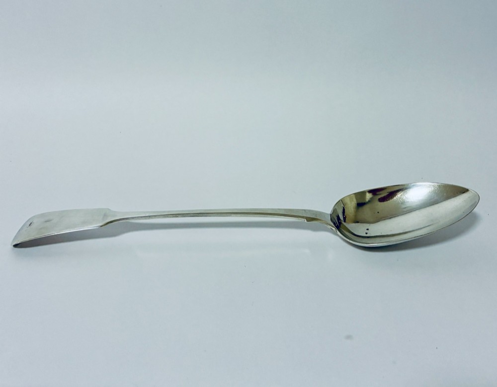 A Georgian sterling silver serving spoon featuring a polished oval bowl and a classic fiddle pattern handle resting against a plain light background.