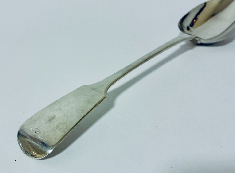 A Georgian sterling silver serving spoon featuring a polished oval bowl and a classic fiddle pattern handle resting against a plain light background. View IV