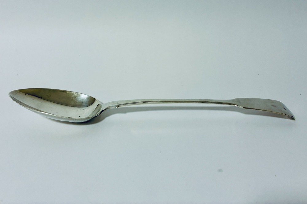 A Georgian sterling silver serving spoon featuring a polished oval bowl and a classic fiddle pattern handle resting against a plain light background. View V