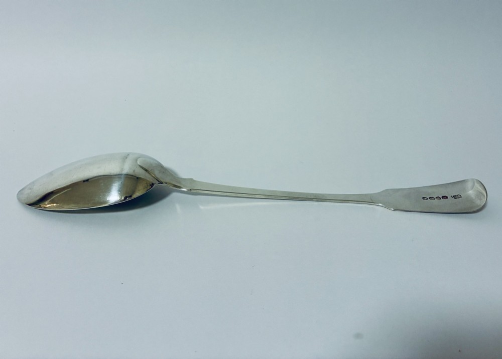 A Georgian sterling silver serving spoon featuring a polished oval bowl and a classic fiddle pattern handle resting against a plain light background. View VII