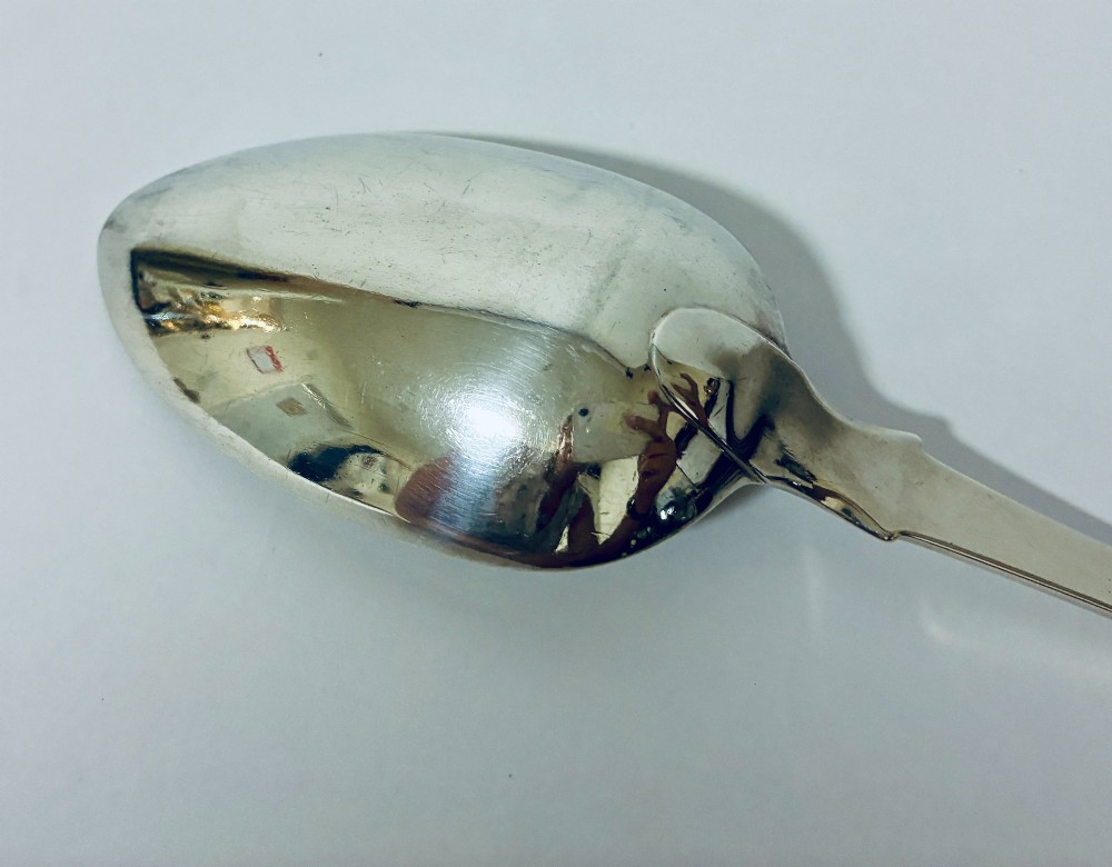 A Georgian sterling silver serving spoon featuring a polished oval bowl and a classic fiddle pattern handle resting against a plain light background. View IX