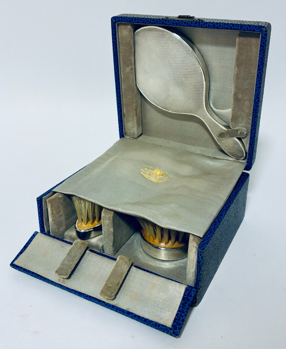 An open blue fitted presentation case displaying two silver-mounted brushes with light-coloured natural bristles against a grey velvet interior. View II