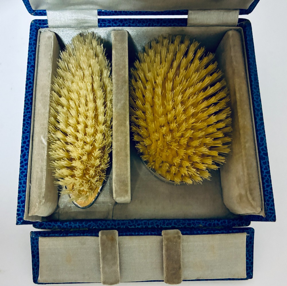 An open blue fitted presentation case displaying two silver-mounted brushes with light-coloured natural bristles against a grey velvet interior. View IV