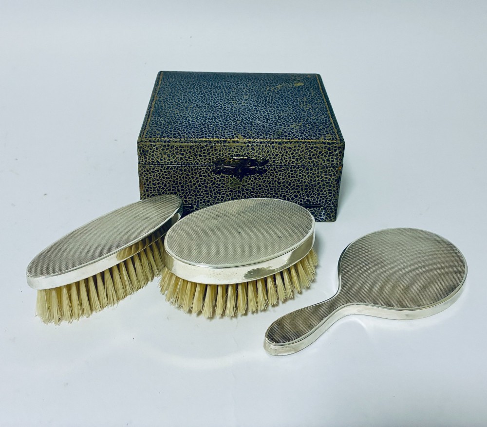 An open blue fitted presentation case displaying two silver-mounted brushes with light-coloured natural bristles against a grey velvet interior. View V